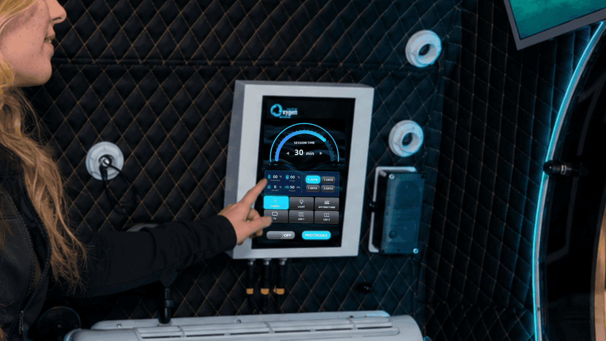 Intuitive high-definition internal touchscreen user interface mounted inside the chamber — showing session timer, real-time temperature, oxygen, humidity and pressure readouts, one-touch ATA pressure selection, and chamber controls